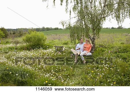 Stock Photo - A couple talking and enjoying a glass of wine on a bench in their backyard. Fotosearch