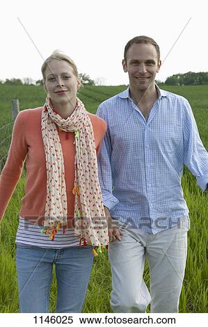 A couple walking hand in hand in a field View Large Photo Image Stock Photography - A couple walking hand in hand in a field. Fotosearch