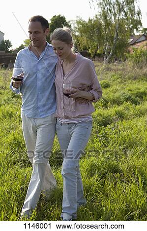 Stock Image - A couple walking outdoors arm in arm with red wine. Fotosearch