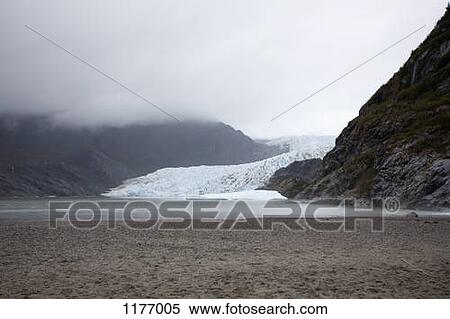 Stock Photography - A distant person standing on a beach near Mendenhall Glacier, Alaska. Fotosearch