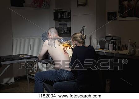 A female tattoo artist tattooing a man's back in a tattoo shop View Large Photo Image Picture - A female tattoo artist tattooing a man's back in a tattoo shop. Fotosearch