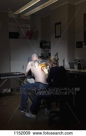 A female tattoo artist tattooing a man's back in a tattoo shop View Large Photo Image Stock Photo - A female tattoo artist tattooing a man's back in a tattoo shop. Fotosearch