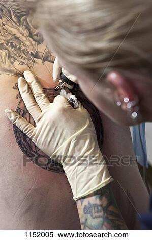 A female tattoo artist tattooing a design on a man's back, over the shoulder view View Large Photo Image Stock Photography - A female tattoo artist tattooing a design on a man's back, over the shoulder view. Fotosearch