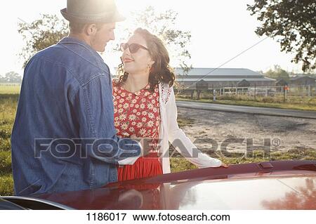 Stock Photo - A flirtatious rockabilly couple standing next to a vintage car. Fotosearch