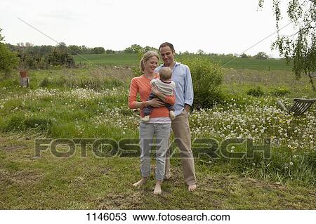 Stock Image - A man and a woman holding a baby standing in their backyard. Fotosearch