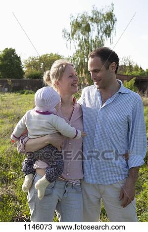 A man and a woman holding a baby standing in their backyard View Large Photo Image Stock Image - A man and a woman holding a baby standing in their backyard. Fotosearch