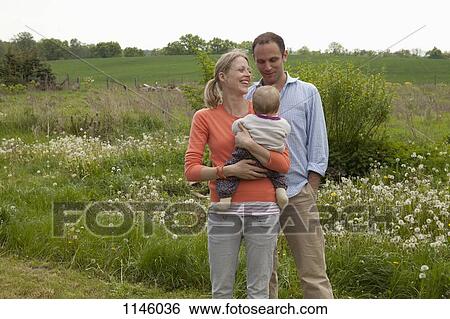 A man and a woman holding a baby standing in their backyard View Large Photo Image Stock Photograph - A man and a woman holding a baby standing in their backyard. Fotosearch