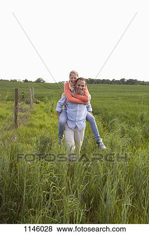 Stock Photo - A man giving his girlfriend a piggy back ride through a field. Fotosearch