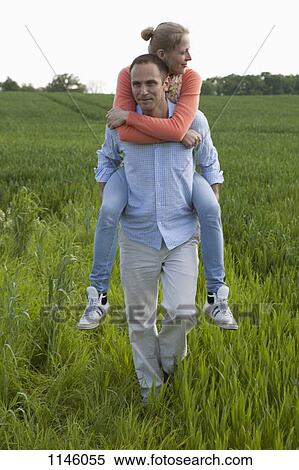 Stock Photography - A man giving his girlfriend a piggy back ride through a field. Fotosearch