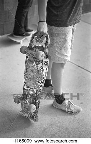 Stock Photo - A man holding a skateboard, waist down. Fotosearch