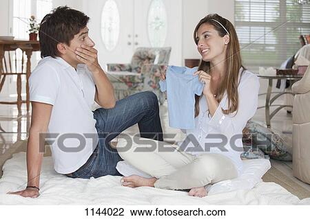 A man looking shocked at the blue baby shirt his girlfriend is showing him View Large Photo Image Stock Image - A man looking shocked at the blue baby shirt his girlfriend is showing him. Fotosearch