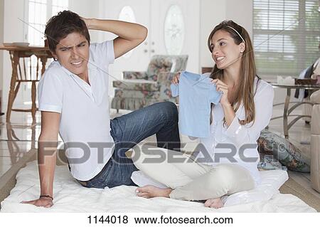 A man looking uncertain at the blue baby shirt his girlfriend is showing him View Large Photo Image Stock Photo - A man looking uncertain at the blue baby shirt his girlfriend is showing him. Fotosearch