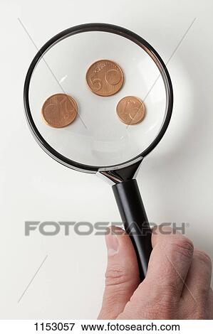 Stock Photo - A man magnifying three copper Euro coins, close-up of hand. Fotosearch