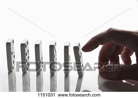 Stock Image - A man pushing the first domino in a row, focus on hand. Fotosearch