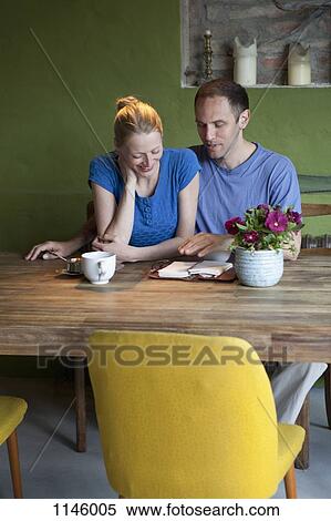 Stock Photography - A man talking about his journal to his girlfriend at the dining table. Fotosearch