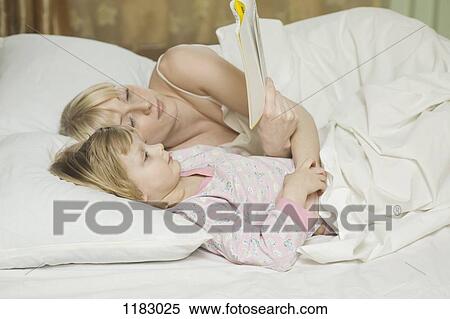 A mother and her young daughter lying in bed, reading a book View Large Photo Image Stock Photography - A mother and her young daughter lying in bed, reading a book. Fotosearch