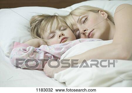 Stock Image - A mother and her young daughter sleeping a bed side by side. Fotosearch
