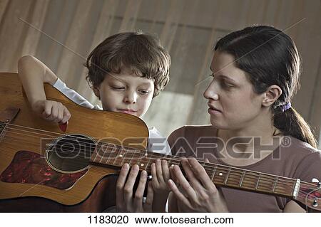 A mother helping her young son with playing an acoustic guitar View Large Photo Image Stock Image - A mother helping her young son with playing an acoustic guitar. Fotosearch
