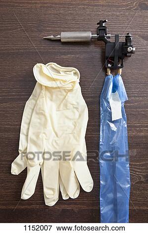 Stock Photo - A pair of surgical gloves next to a tattoo gun on a table, close-up. Fotosearch
