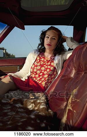 Stock Image - A pretty rockabilly woman sitting in the passenger seat of a vintage car. Fotosearch
