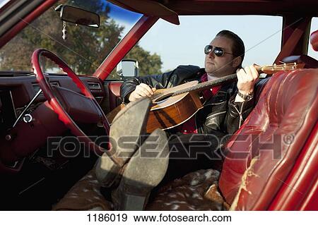 A rockabilly guy playing an acoustic guitar while sitting in his vintage car View Large Photo Image Stock Photo - A rockabilly guy playing an acoustic guitar while sitting in his vintage car. Fotosearch