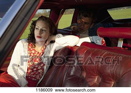 Stock Photo - A rockabilly woman and man sitting in a vintage car. Fotosearch