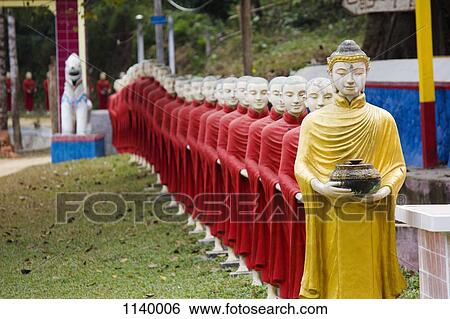 Stock Photograph - A row of Buddhist monk statues in a procession behind a Buddha statue, Hpa-An, Burma. Fotosearch