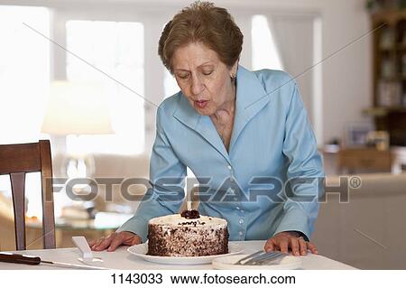 Stock Image - A senior woman blowing out a candle on a cake. Fotosearch