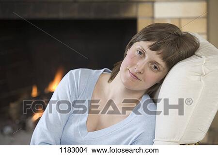 Picture - A serene young woman sitting near a roaring fire. Fotosearch