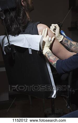 Stock Image - A tattoo artist preparing to tattoo a man's bare arm. Fotosearch