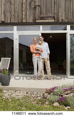 Stock Image - A woman and man and their baby standing in front of their house. Fotosearch