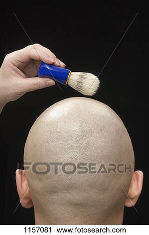 Stock Image - A woman holding a shaving brush above the shaved head of a man. Fotosearch