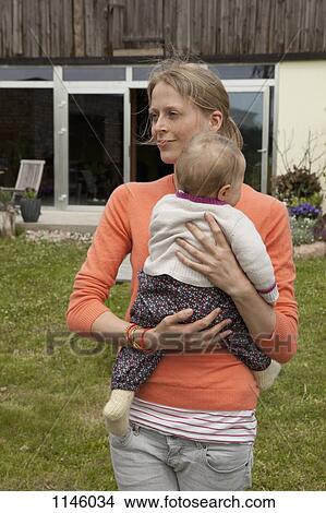 Picture - A woman holding her baby in her backyard. Fotosearch