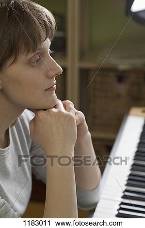 Stock Image - A woman leaning on an upright piano, looking pensive. Fotosearch