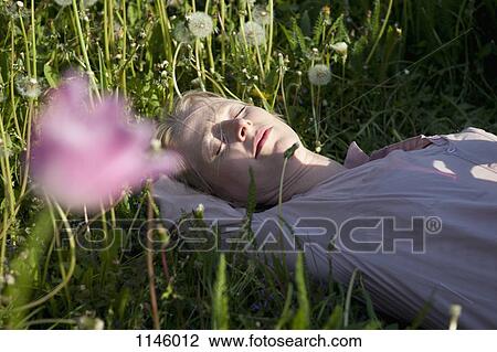 Stock Image - A woman lying in the grass sleeping, close-up. Fotosearch