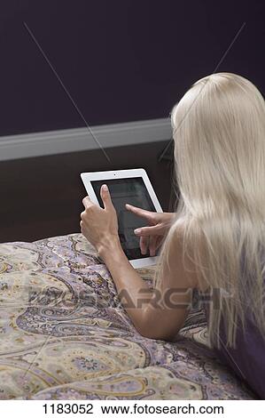 A woman lying on a bed, using a digital tablet View Large Photo Image Stock Image - A woman lying on a bed, using a digital tablet. Fotosearch