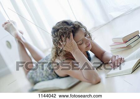 Stock Image - A woman lying on a floor reading a book. Fotosearch