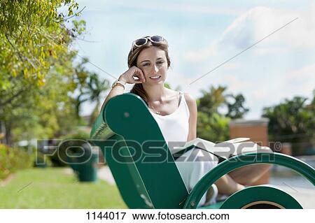A woman relaxing on a park bench with a book View Large Photo Image Stock Photo - A woman relaxing on a park bench with a book . Fotosearch