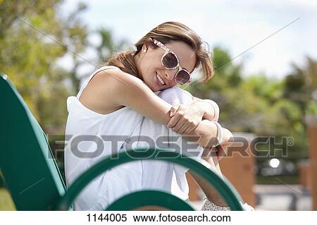 A woman sitting on a park bench, smiling at the camera View Large Photo Image Stock Photography - A woman sitting on a park bench, smiling at the camera. Fotosearch