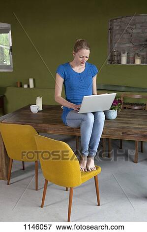 A woman sitting on her dining table using a laptop View Large Photo Image Stock Photo - A woman sitting on her dining table using a laptop. Fotosearch