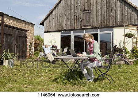 A woman using a laptop and having breakfast in her backyard View Large Photo Image Picture - A woman using a laptop and having breakfast in her backyard. Fotosearch