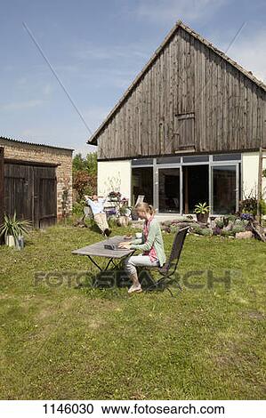 Stock Image - A woman using a laptop and having breakfast in her backyard. Fotosearch