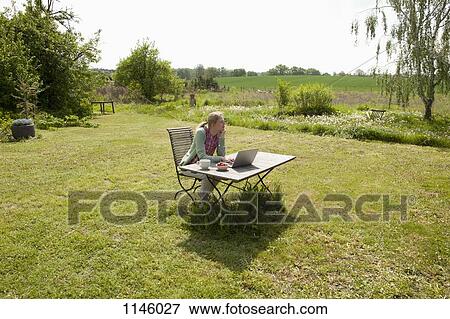A woman with a laptop sitting at a table in her back yard, rural setting View Large Photo Image Stock Photo - A woman with a laptop sitting at a table in her back yard, rural setting. Fotosearch