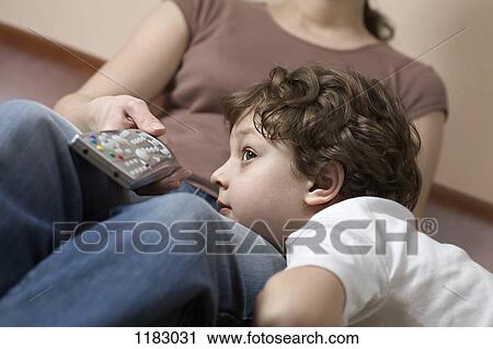 Stock Image - A young boy resting his head on his mom's leg, watching TV. Fotosearch