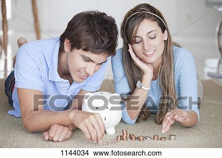 Picture - A young cheerful couple counting coins on the floor. Fotosearch