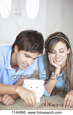 Stock Image - A young cheerful couple counting coins on the floor. Fotosearch