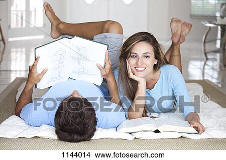 A young couple lying on the floor studying with textbooks View Large Photo Image Picture - A young couple lying on the floor studying with textbooks. Fotosearch