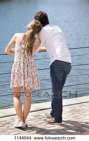 Picture - A young couple standing at a railing enjoying the lake view. Fotosearch