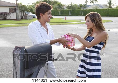 Stock Image - A young couple standing by mailbox, playfully fighting over a gift. Fotosearch
