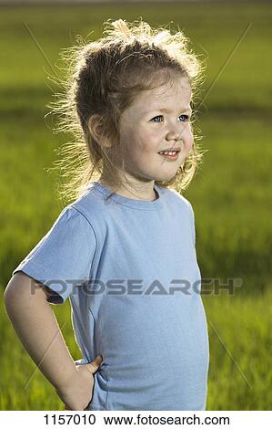 Stock Image - A young girl standing in a field and looking away. Fotosearch